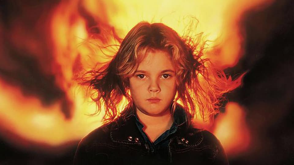 Firestarter 1984 screenplay feature image with Drew Barrymore standing facing the camera with a huge fire behind.