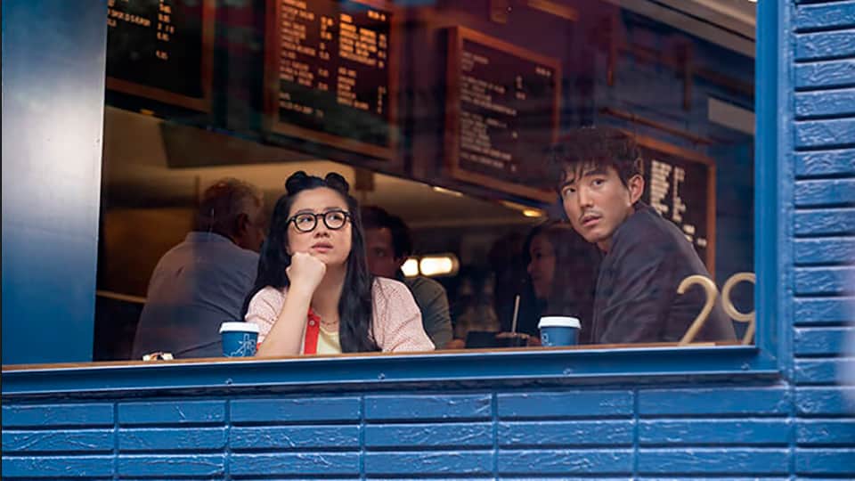 Shortcomings screenplay hero image with Justin H. Min and Sherry Cola set against a coffee shop background, and staring out a window.