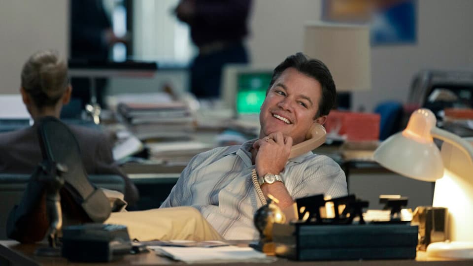 Air screenplay hero image with Matt Damon, sitting in an 1980s-era office, holding a telephone receiver to his ear and smiling.